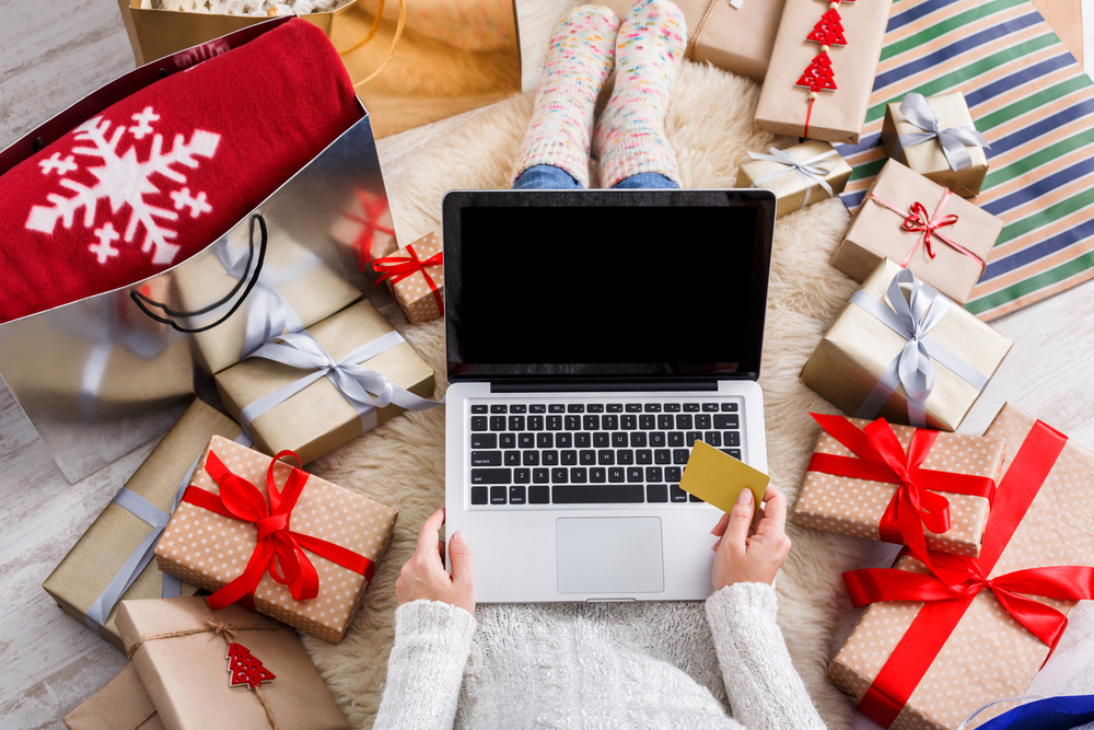 Woman shopping online surrounded by holiday gifts