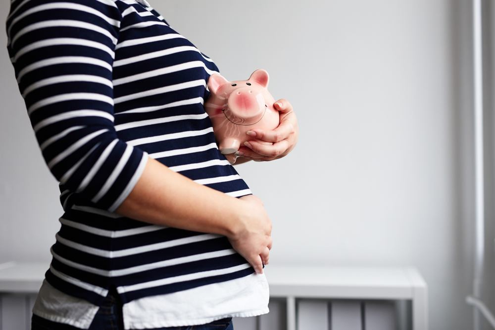 Woman Holding a Piggy Bank Against Her Pregnant Belly
