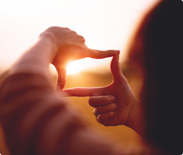 Woman's hands forming a rectangular frame against a sunset